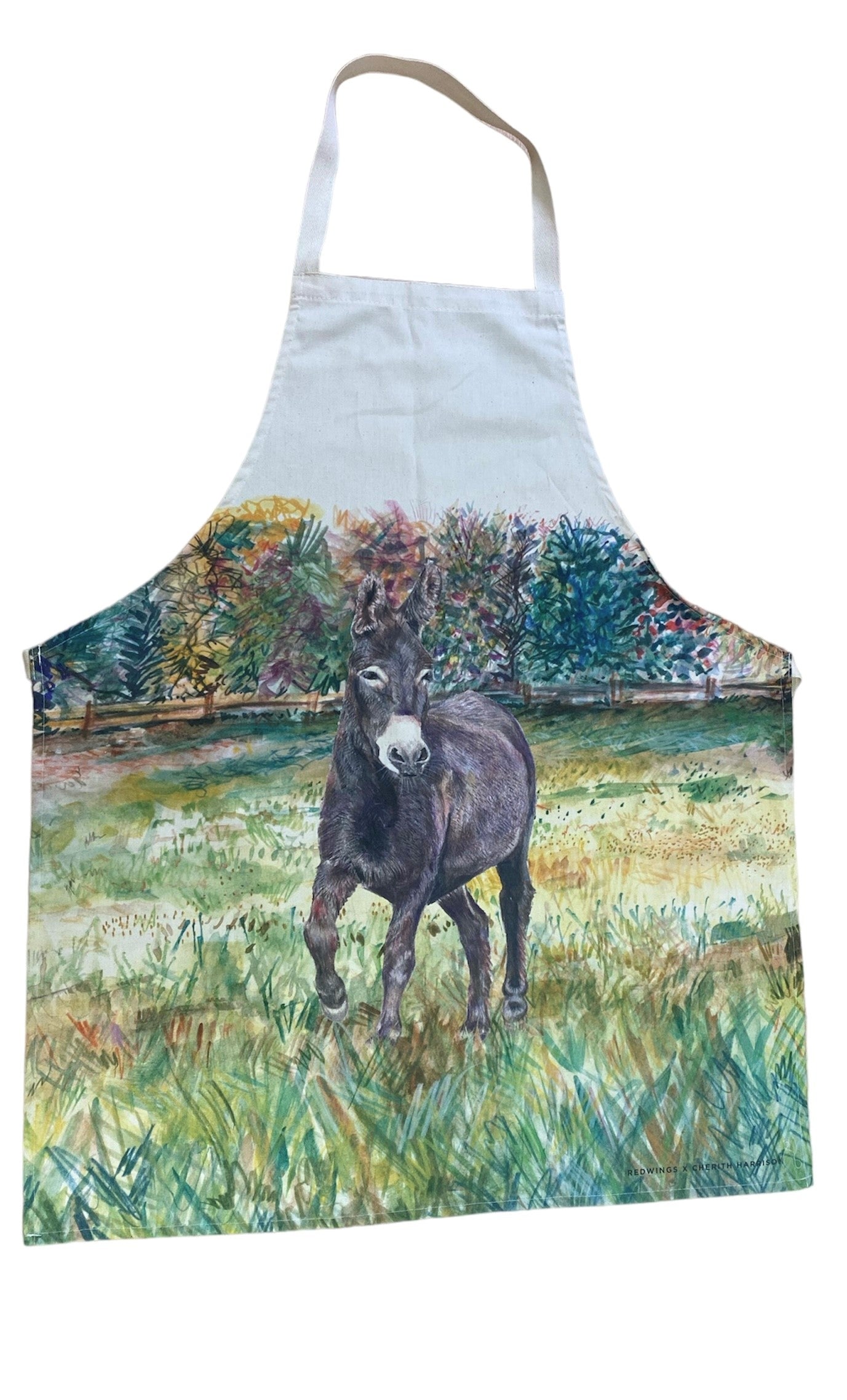 Image shows a cream cotton apron with a beautifully drawn image of our brown Denver the donkey standing in a grassy field