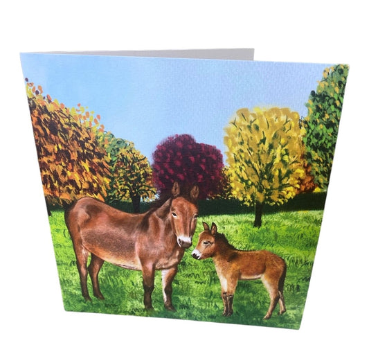 Image shows a square greetings card with a beautifully drawn image of our brown mule muffin standing in a grassy field with a line of autumnal colour trees