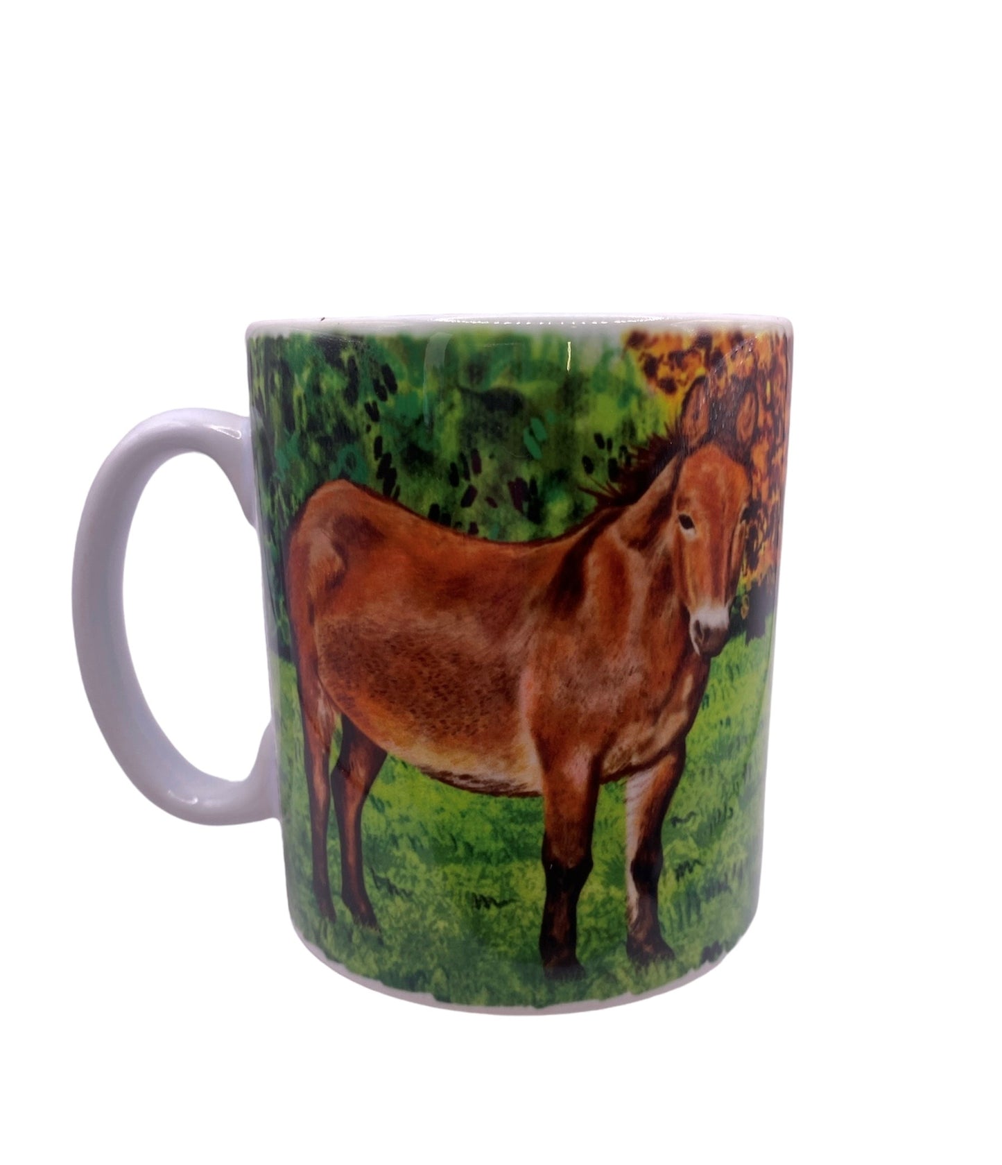 Image shows a white handled mug with a beautifully drawn image of our brown mule muffin standing in a grassy field with a line of autumnal colour trees which wraps around the mug