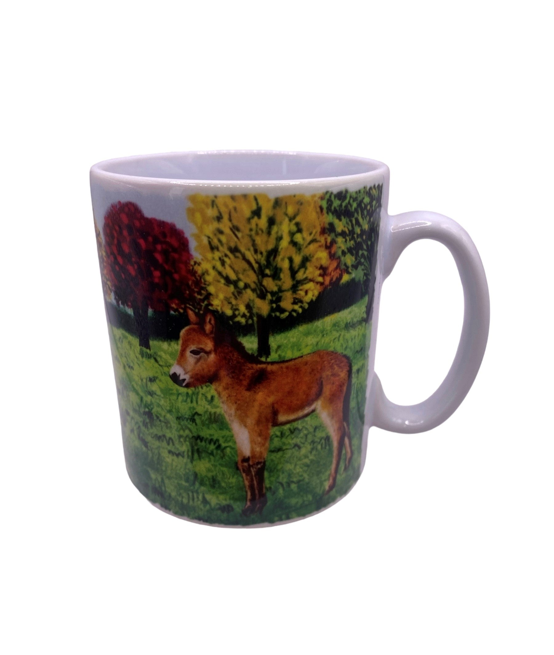 Image shows a white handled mug with a beautifully drawn image of our brown mule muffin standing in a grassy field with a line of autumnal colour trees which wraps around the mug