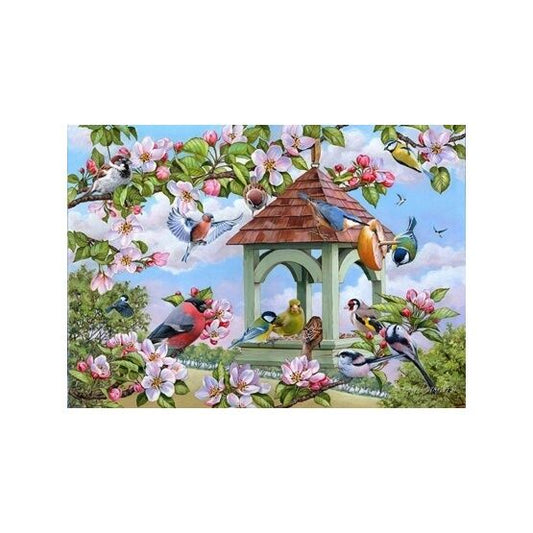 Image shows a green wooden bird stand with a variety of colourful birds eating and resting with some beautiful pink and white flowers on a tree branch